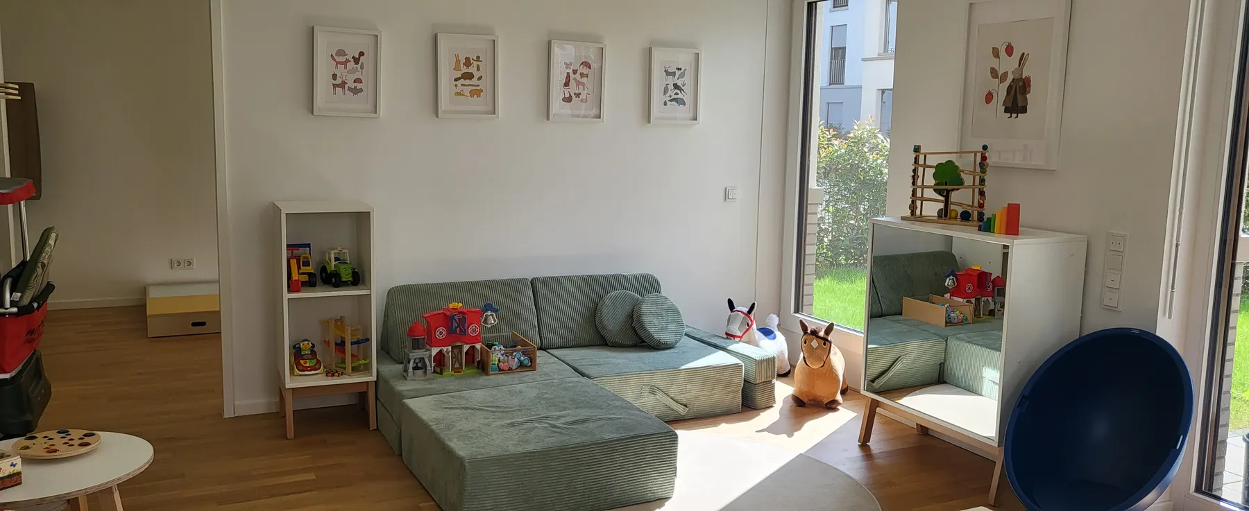 Heller Spielraum mit Salbeigrün-Sofa, Spielsachen und Blick in den Garten