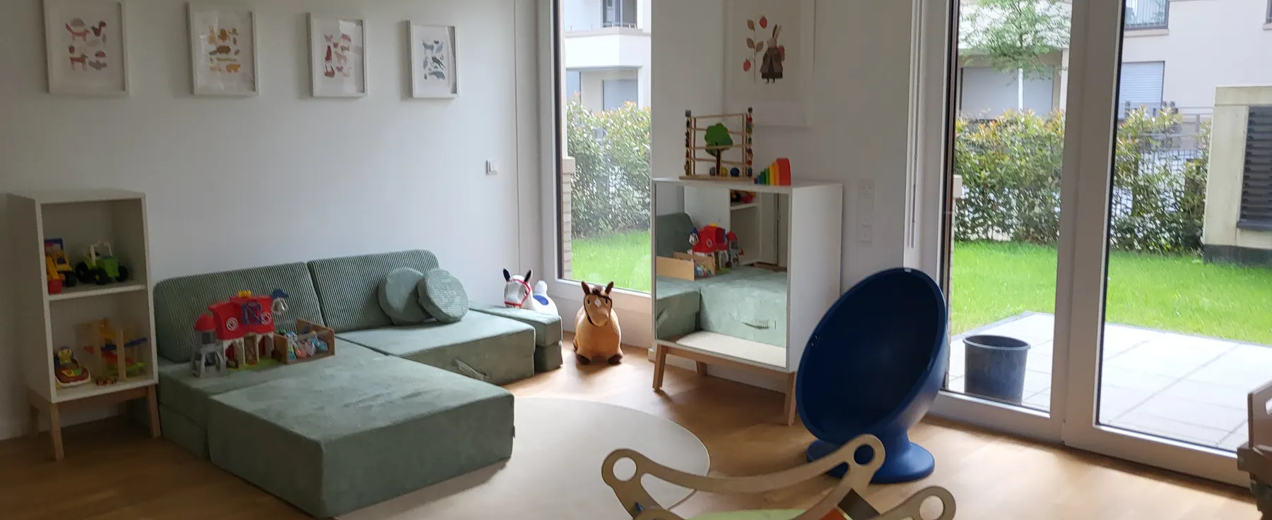 Heller Spielbereich mit Salbeigrün-Sofa und großen Fenstern zum Garten